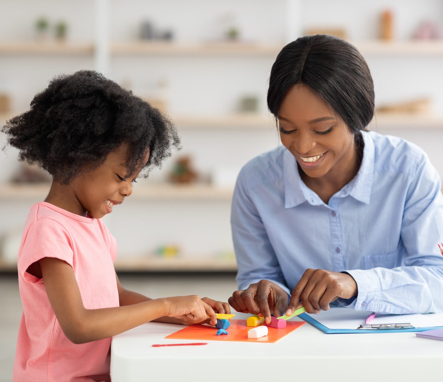 Adorable little black girl and teacher playing with play dough