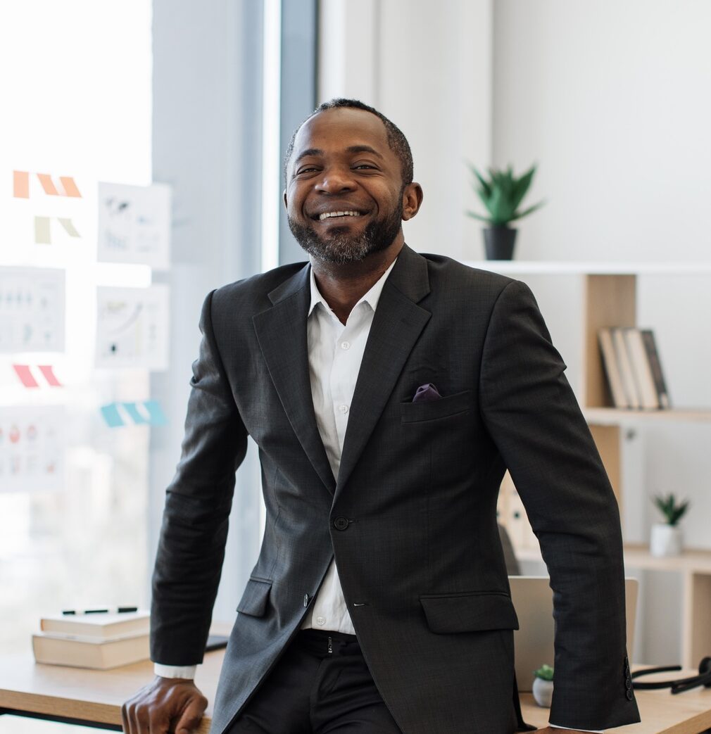 Company leader resting on edge of office desk