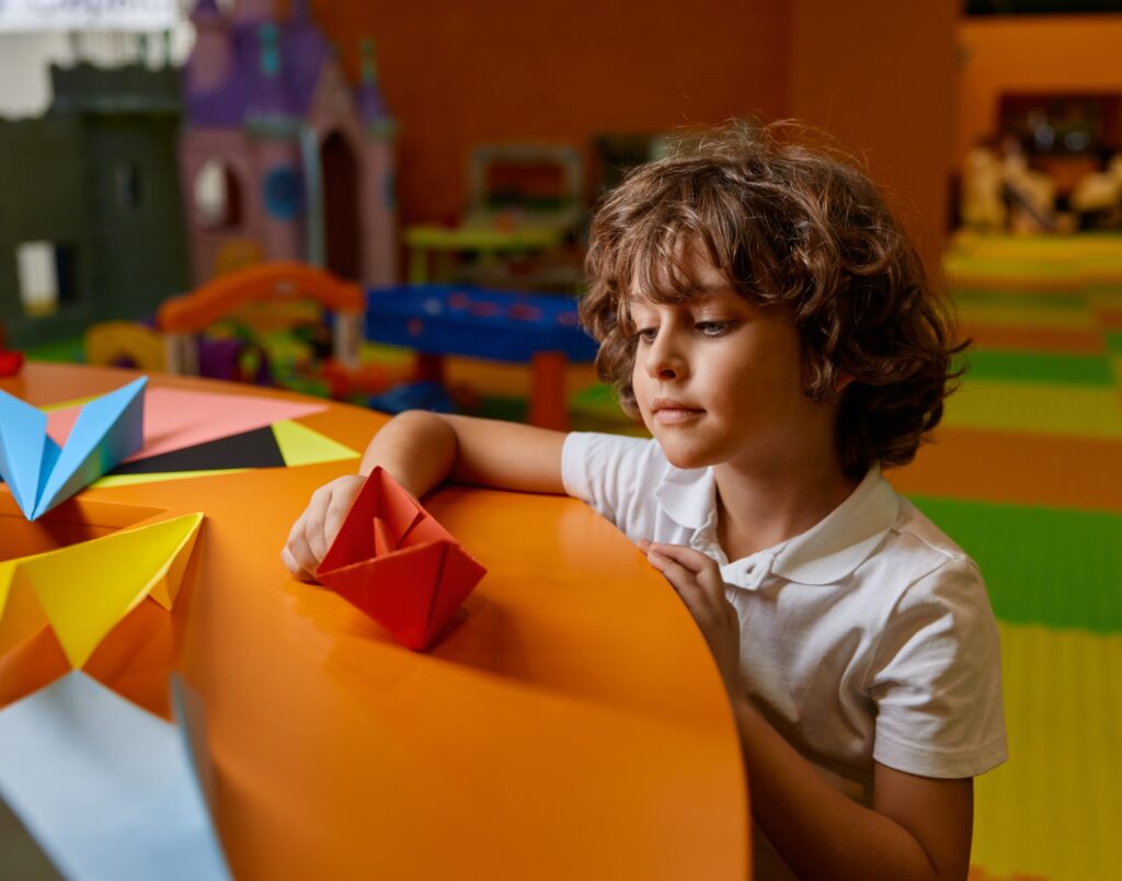 Cute boy child playing handmade origami paper boat at childcare center