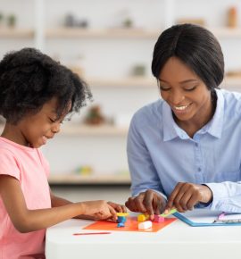 Adorable little black girl and teacher playing with play dough