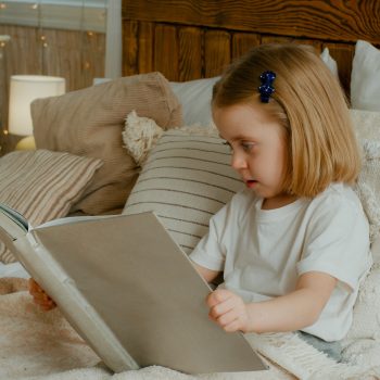 Cute little 5s Caucasian alone child girl daughter looking in book kid preschool baby sitting in bed